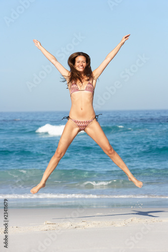 Athletic Young Woman Jumping On Sandy Beach On Holiday Wearing B