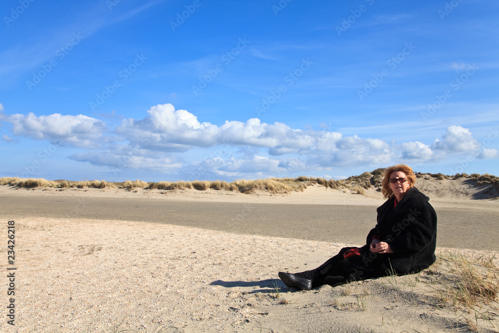 Woman with dog sitting in the sand dunes on the beach
