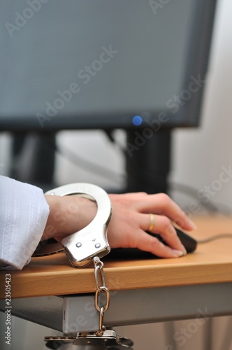 Business person tied with handcuffs to workplace