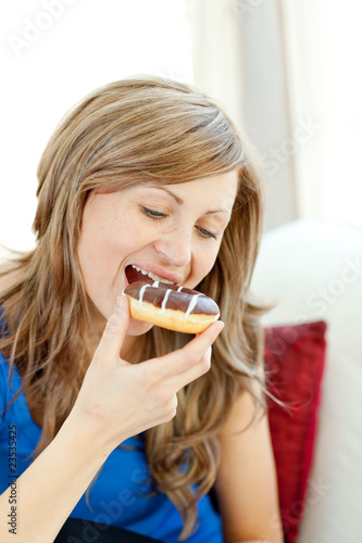 Radiant woman is eating a donut on a sofa
