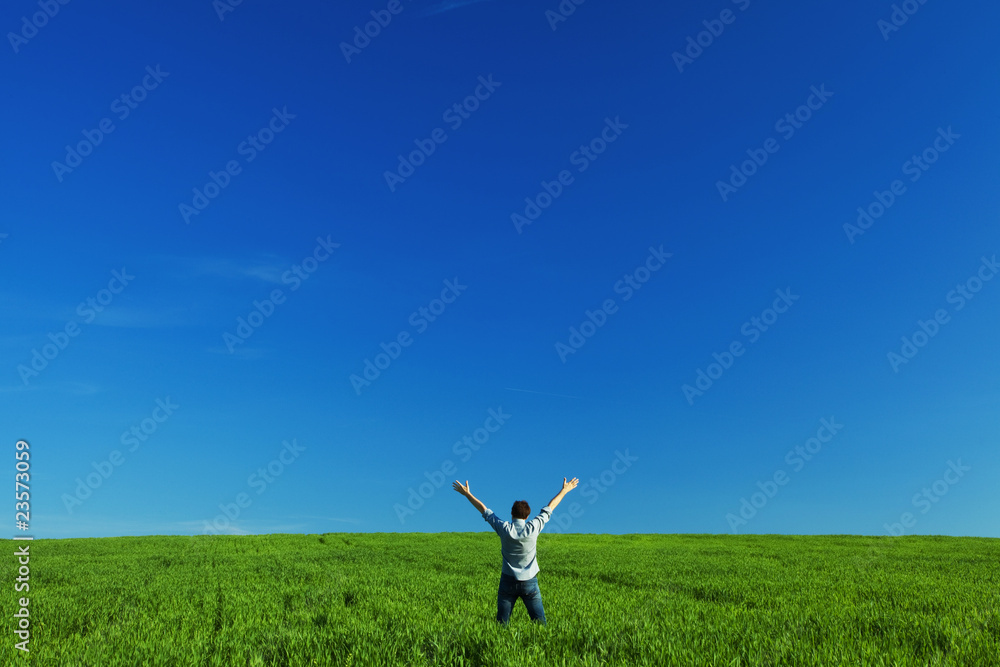 young man outstretched arms in green field against the blue sky young man outstretched arms in green field against the blue sky