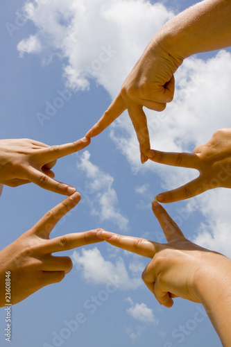 Many hands connecting to star shape under sky