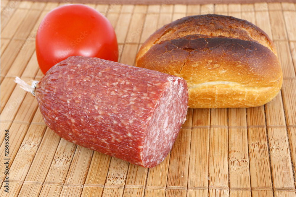 roll bread , salami and tomato on the table