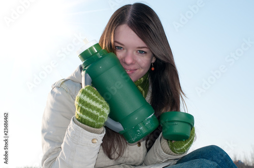 Girl on winter picnic with cup of hot tee and thermos