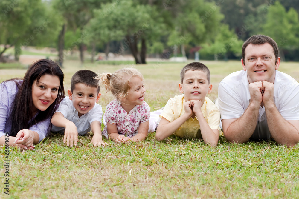 Cheerful family of five lying on lawn in the green park Cheerful family of five lying on lawn in the green park