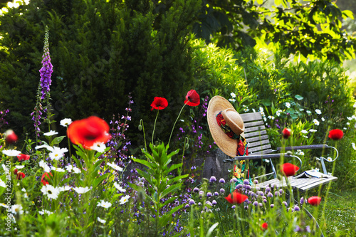 Fototapeta Naklejka Na Ścianę i Meble -  garden bench with straw hat within summer flowers 02