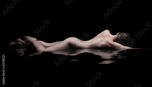 Nude woman lies in water, low key