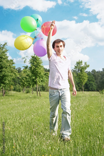 young man with many colored balloons at green summer lawn