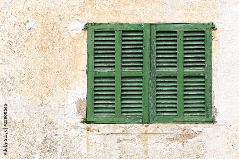 Single window with closed green shutters on a weathered facade i