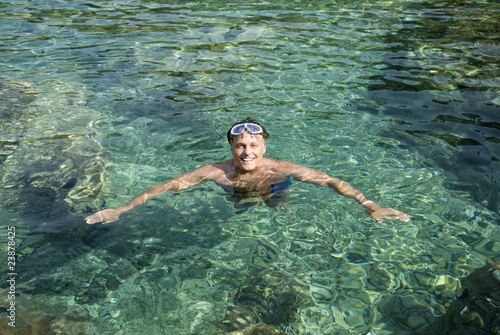 color photo of a happy smiling man in clear blue water.