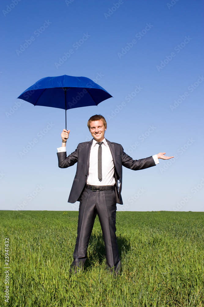 Image of young businessman with blue umbrella in field Image of young businessman with blue umbrella in field