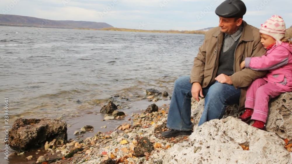 daddy with daughter sit on stone on river bank daddy with daughter sit on stone on river bank