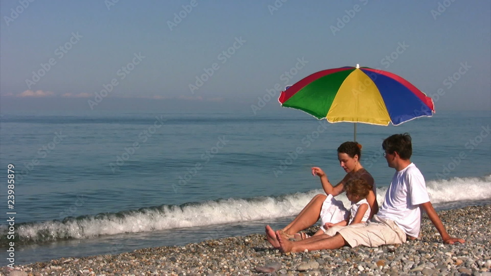 family sits near beach umbrella family sits near beach umbrella