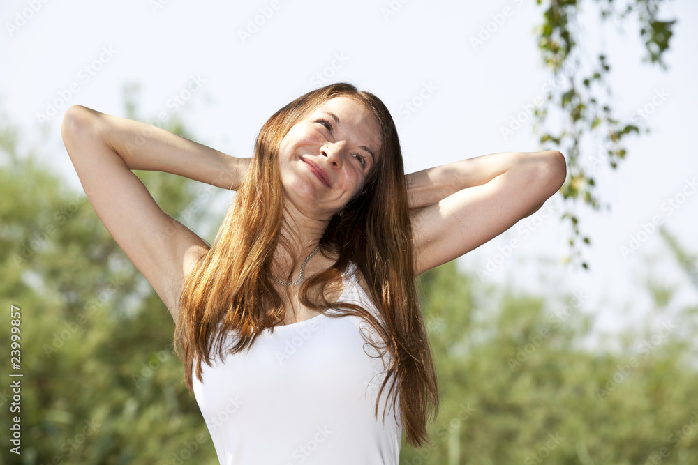 lächelnde hübsche junge Frau posiert mit Armen hinter dem Kopf