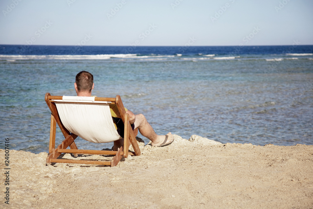 man sit on chaise and look at sea.