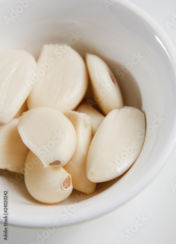 Peeled garlic cloves in white bowl, ready as ingredient.
