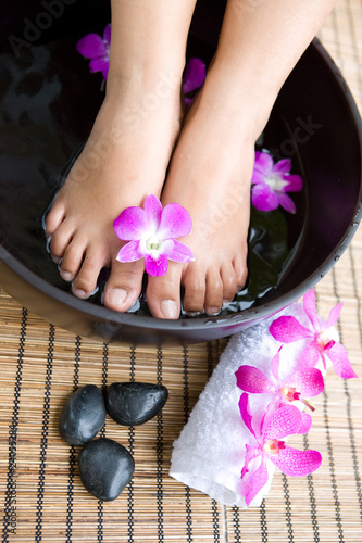 Feminine feet in foot spa bowl with orchids
