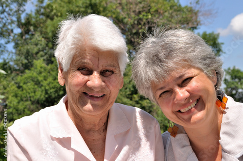 Two elderly women laugh, sitting in nature