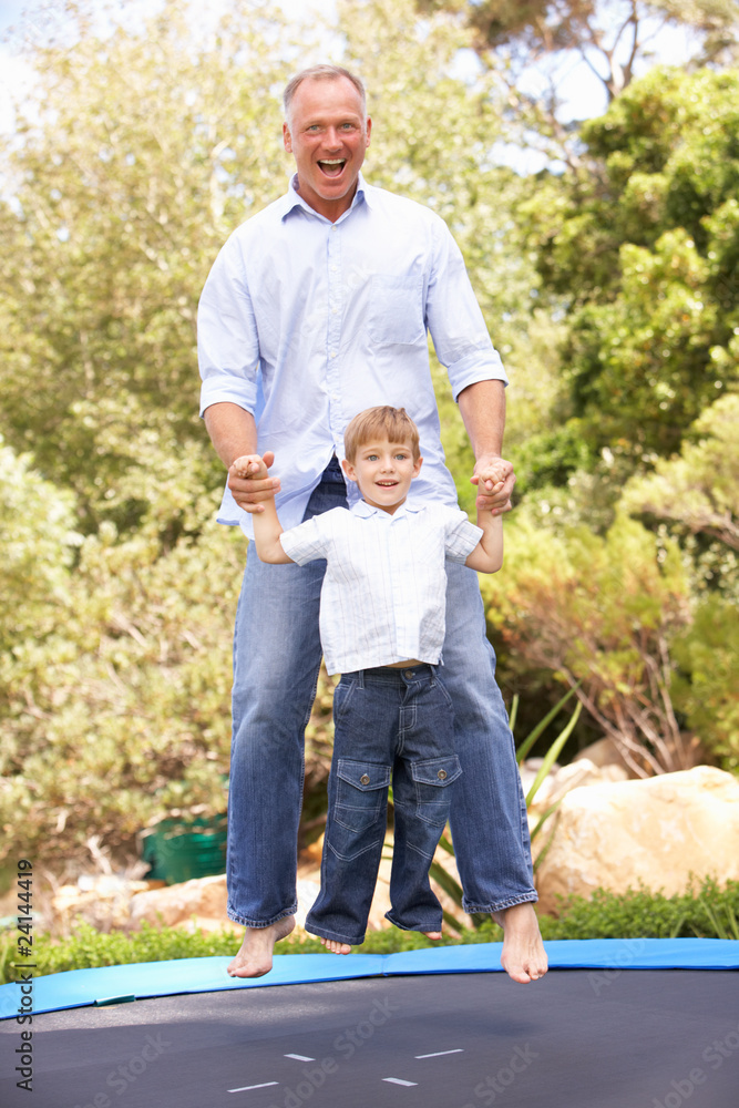 Father And Son Jumping On Trampoline In Garden Father And Son Jumping On Trampoline In Garden