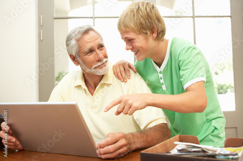 Teenage Grandson Helping Grandfather To Use Laptop At Home