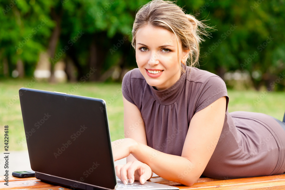 Young pretty woman with laptop lying on the bench in a park Young pretty woman with laptop lying on the bench in a park