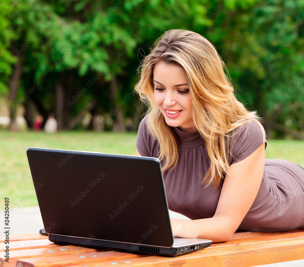 Young pretty woman with laptop lying on the bench in a park Young pretty woman with laptop lying on the bench in a park