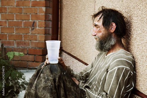 Sad homeless man sitting on at the wall on city street photo