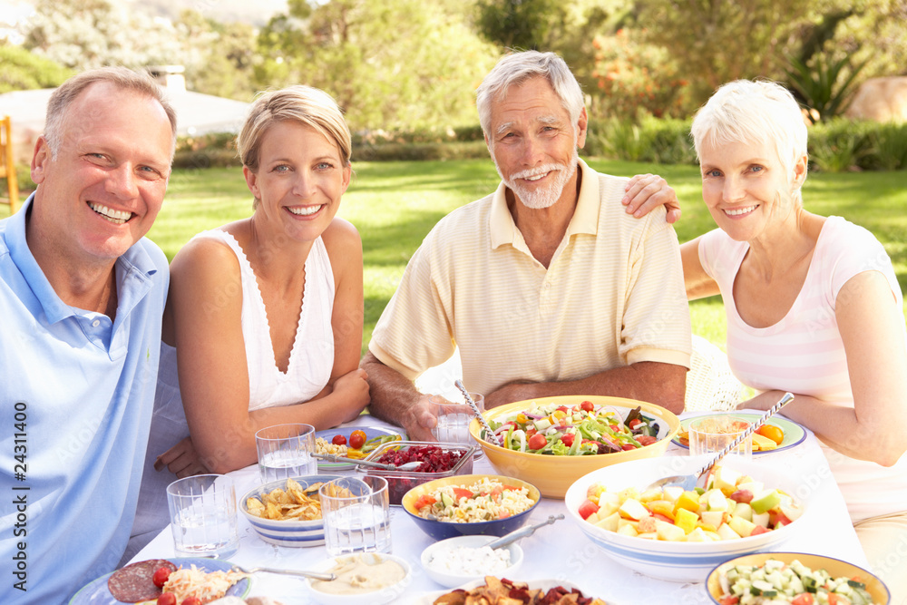 Adult Son And Daughter Enjoying Meal In Garden With Senior Paren Adult Son And Daughter Enjoying Meal In Garden With Senior Paren