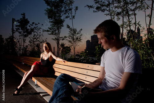 Young attractive couple sit next to each other on a park bench © Donald Bowers