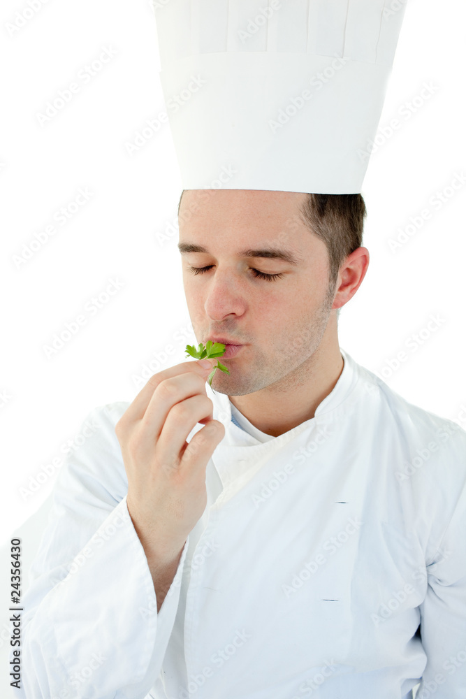 Young cook with closed eyes tasting a herb against white backgro Young cook with closed eyes tasting a herb against white backgro