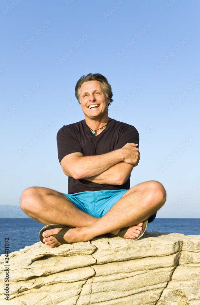 happy smiling forties man sitting on a rock at the beach. happy smiling forties man sitting on a rock at the beach.