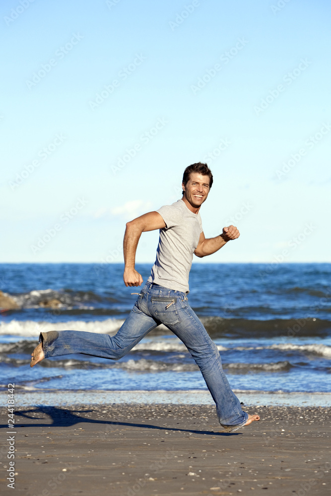 Handsome young man running barefoot on beach in casual wear Handsome young man running barefoot on beach in casual wear