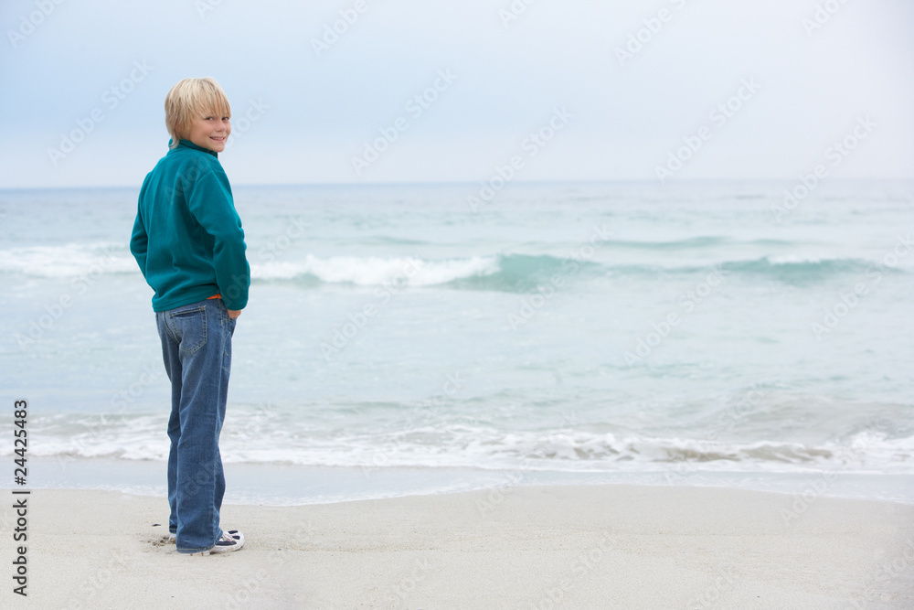 Young Boy On Holiday Standing On Winter Beach Looking Out To Sea Young Boy On Holiday Standing On Winter Beach Looking Out To Sea