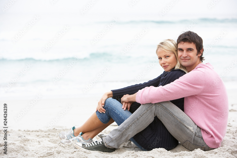Young Couple On Holiday Sitting On Winter Beach