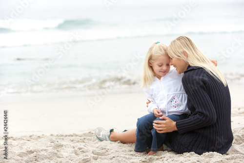 Mother And Daughter On Holiday Sitting On Winter Beach