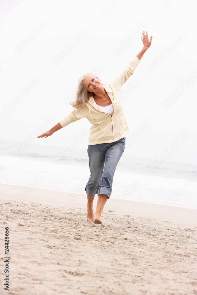 Senior Woman On Holiday Running Along Winter Beach Senior Woman On Holiday Running Along Winter Beach
