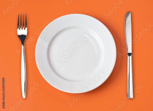Knife  white plate and fork on orange background