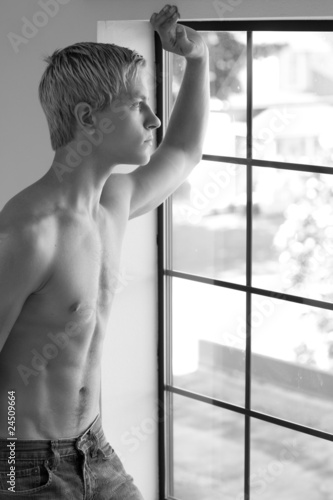 Shirtless young man looking out of the window