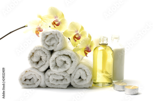 Rolled up white towel, candle, lotion with orchid