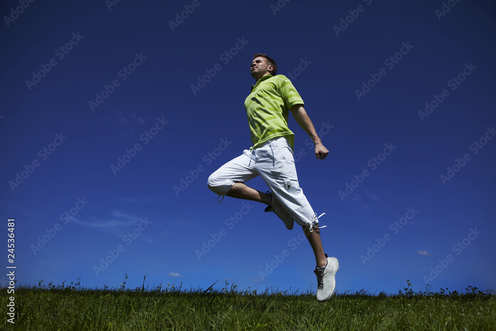 Jumping up guy in a green shirt against blue sky.