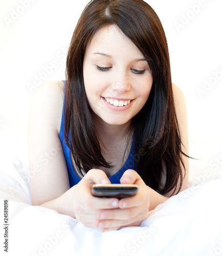 Happy female teenager using cellphone lying on the bed