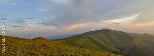 Light blue evening sky above grassy mountain ridge panorama