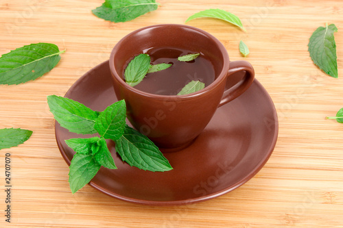 Cup of green tea on the saucer with mint on wooden surface