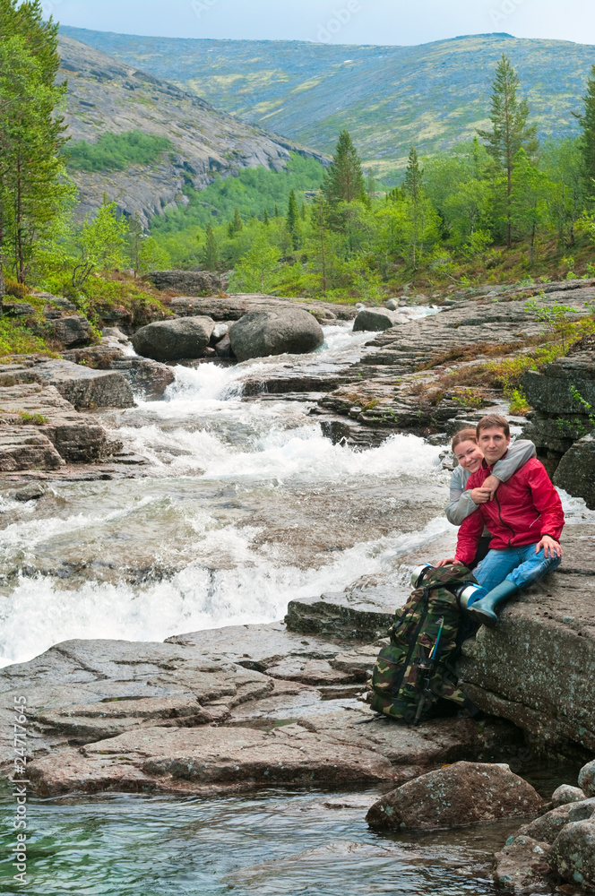 Woman embracing young man near waterfall in mountains