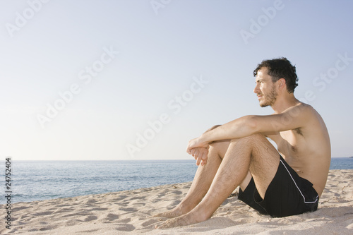 Young man sitting in the sand of a beach - Sardinia, Italy