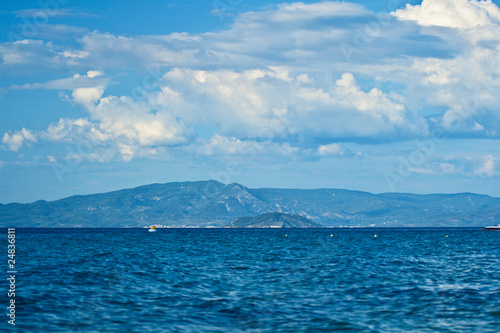 Cloudy sky, blue sea and the mountains in the background.