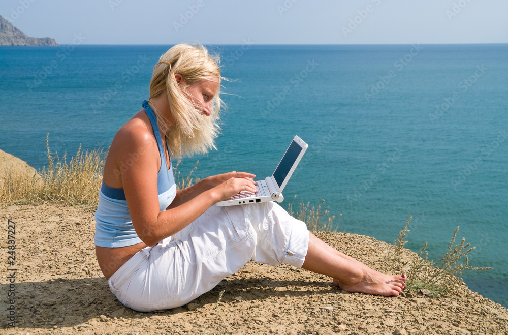 girl with a netbook sitting on the bank against the sky