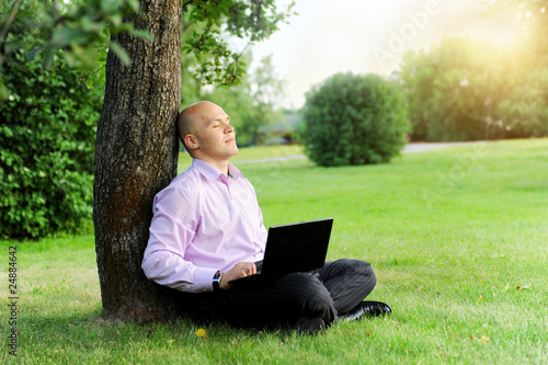 Businessman with laptop sitting near a tree