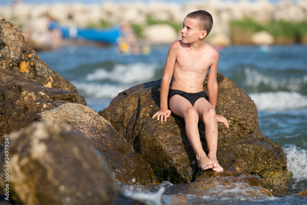 Little boy sitting on rocks at sea Little boy sitting on rocks at sea