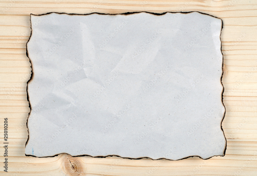 Burned and crumpled paper on  natural wood background.